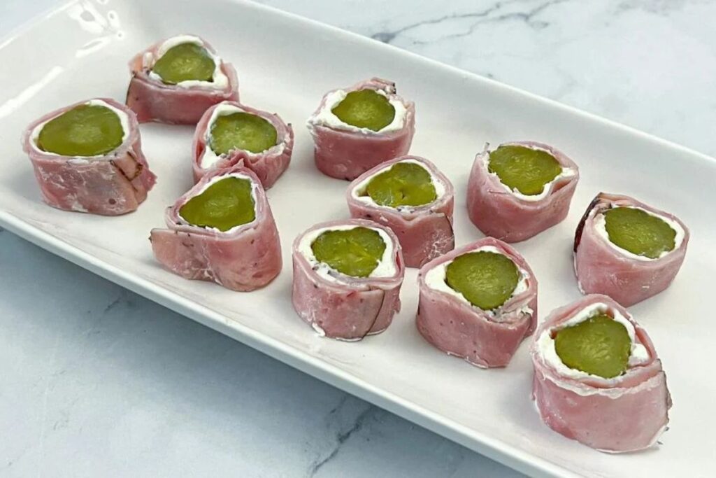Ham roll-ups filled with cream cheese and pickles on a white plate.