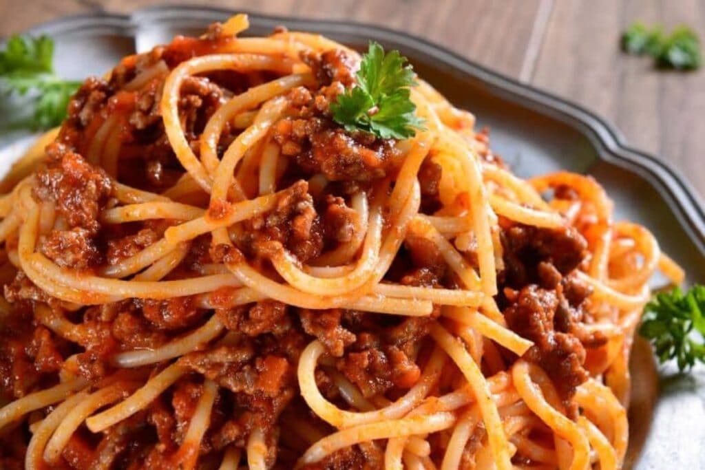 Close-up of spaghetti bolognese with parsley garnish on a silver plate.