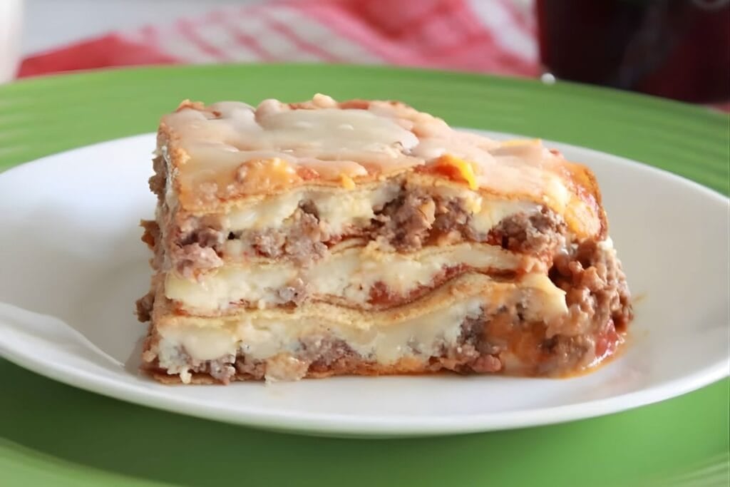 Slice of lasagna with crepini noodles, meat, and cheese on a plate.