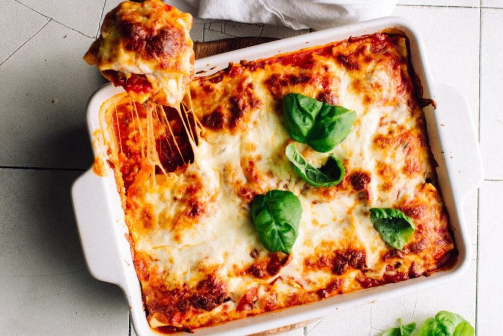 Lasagna in a white baking dish with melted cheese and basil garnish.