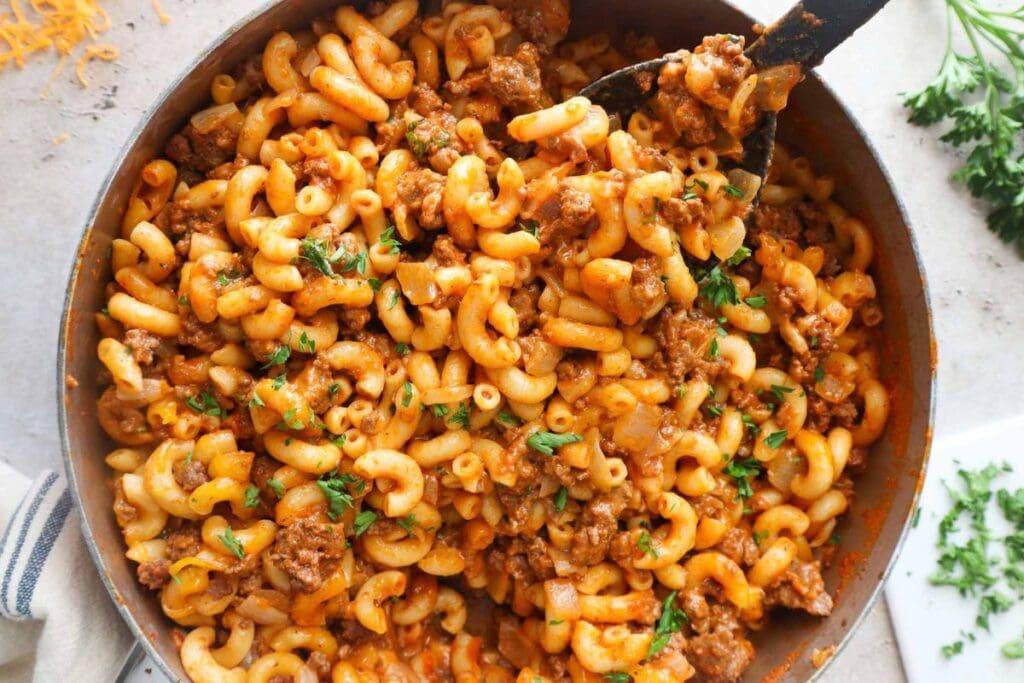 Skillet of macaroni and cheese with ground beef and parsley.