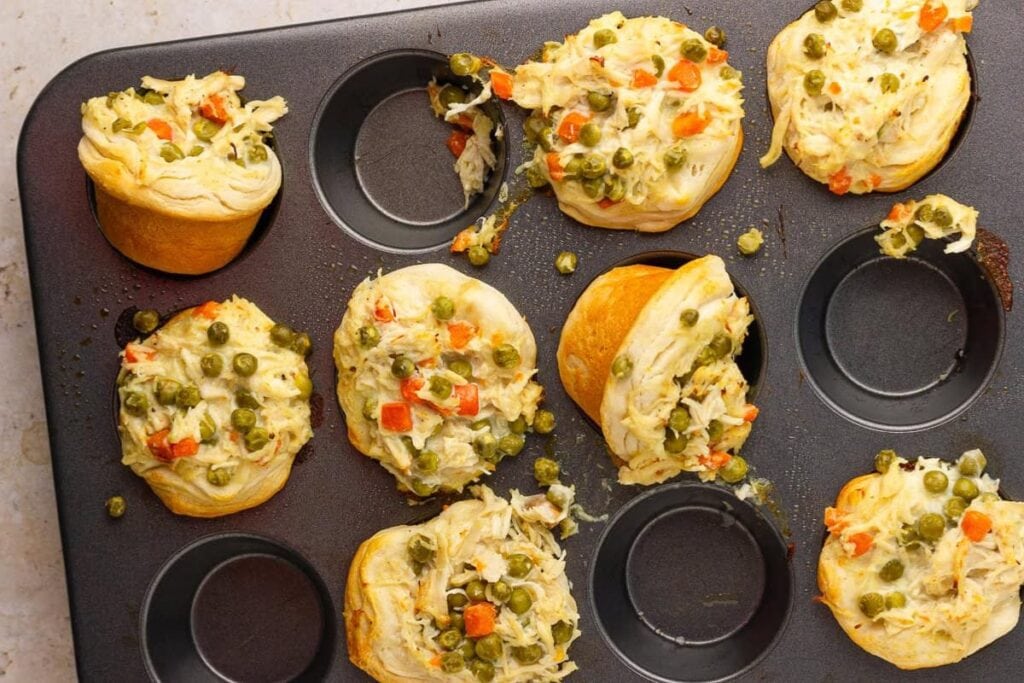 Chicken pot pie bites in a muffin tin with peas and carrots.