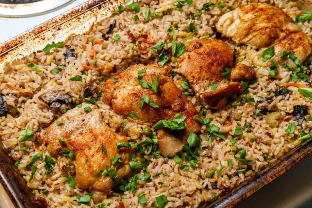 Chicken thighs and rice pilaf on a baking sheet, garnished with parsley.