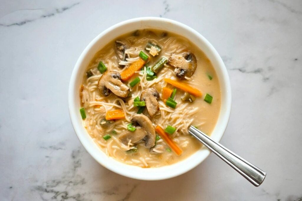 Overhead shot of noodle soup with mushrooms, carrots, and green onions.