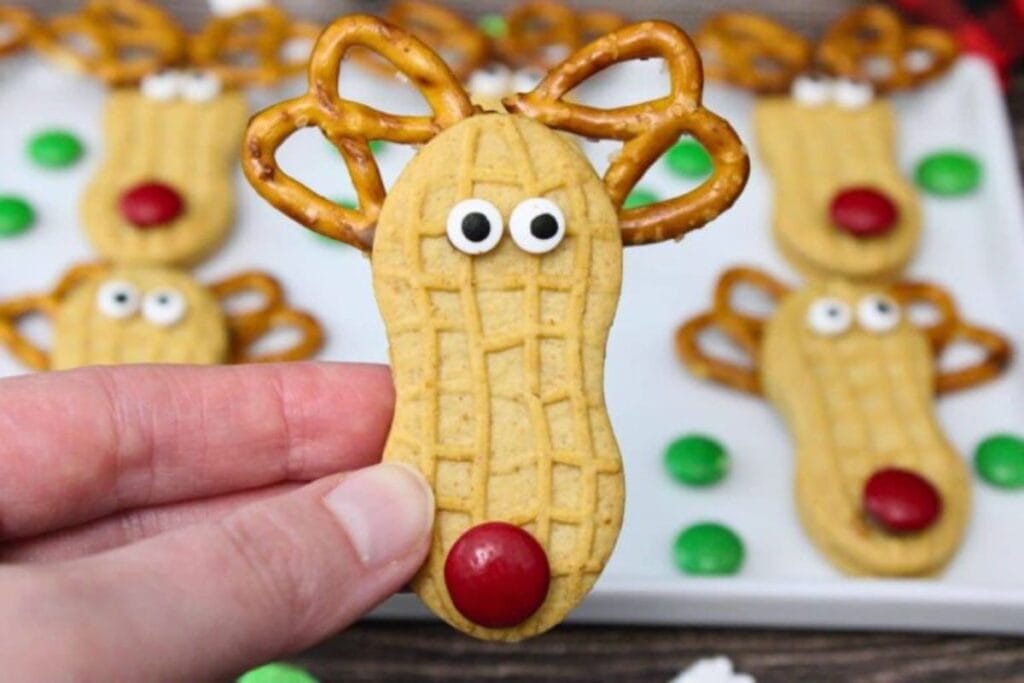 Hand holding a Nutter Butter cookie decorated as a reindeer with pretzel antlers.