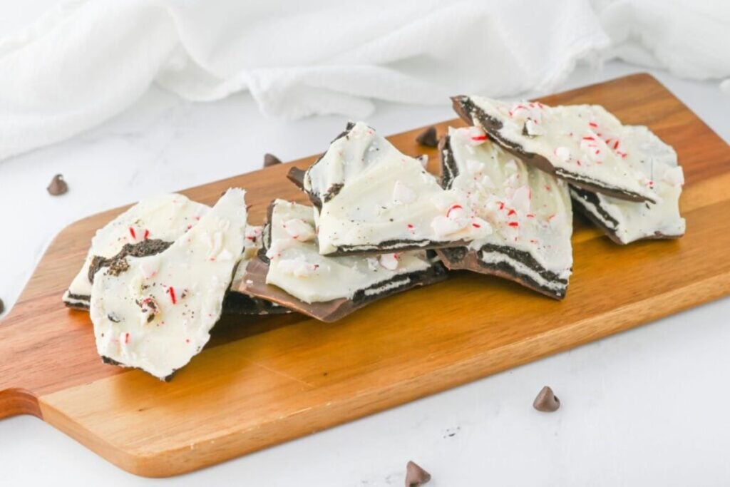Oreo peppermint bark pieces on a wooden board with chocolate chips scattered around.