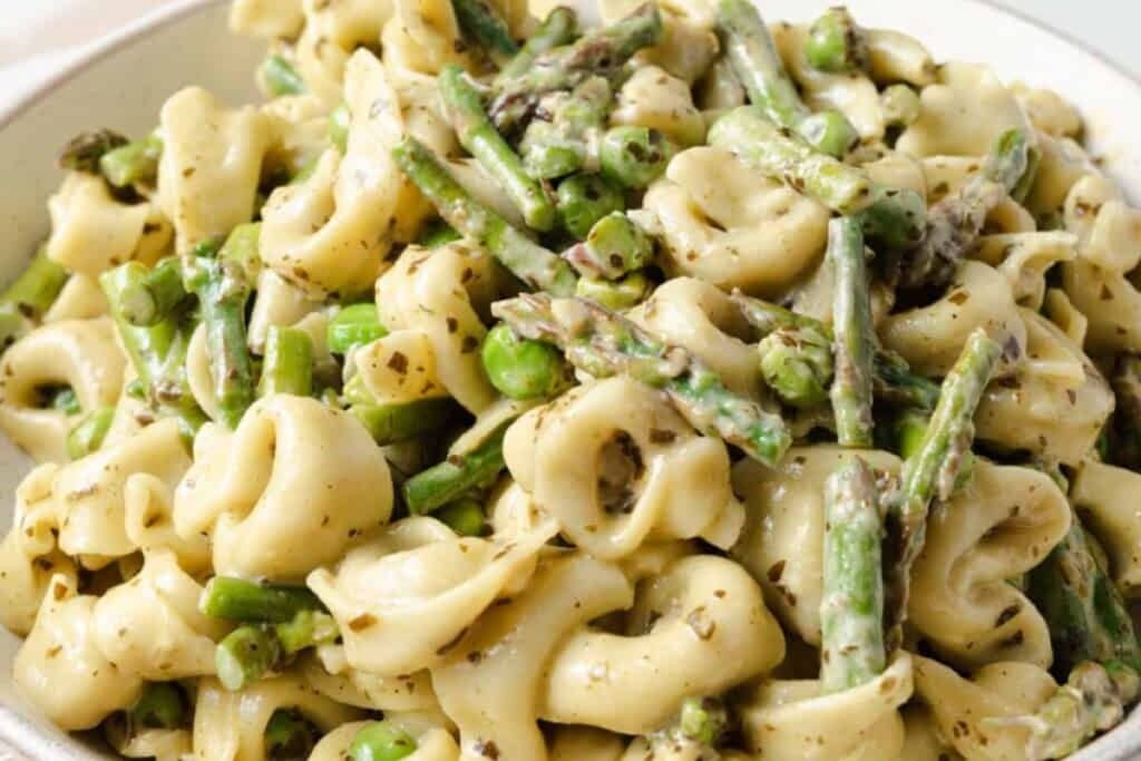 Close-up of tortellini pasta with pesto, asparagus, and peas.