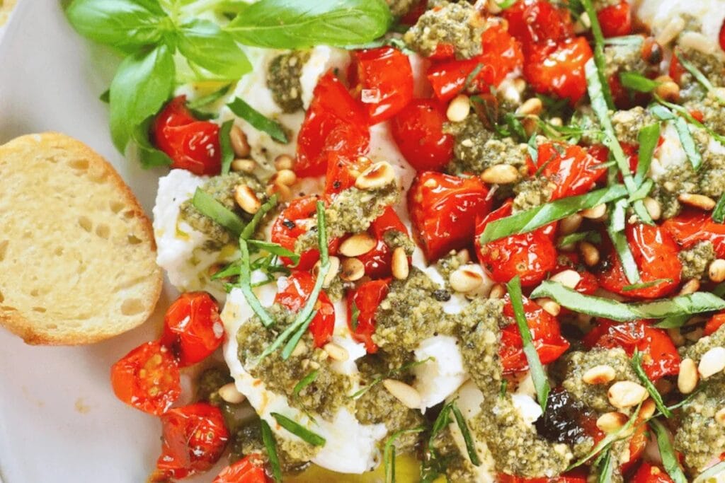 Burrata appetizer with roasted tomatoes, pesto, pine nuts, basil, and toasted bread.