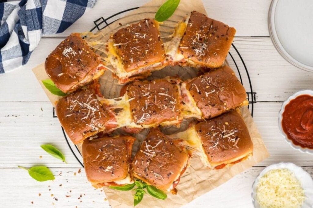 Overhead shot of baked pizza sliders with melted cheese and basil.