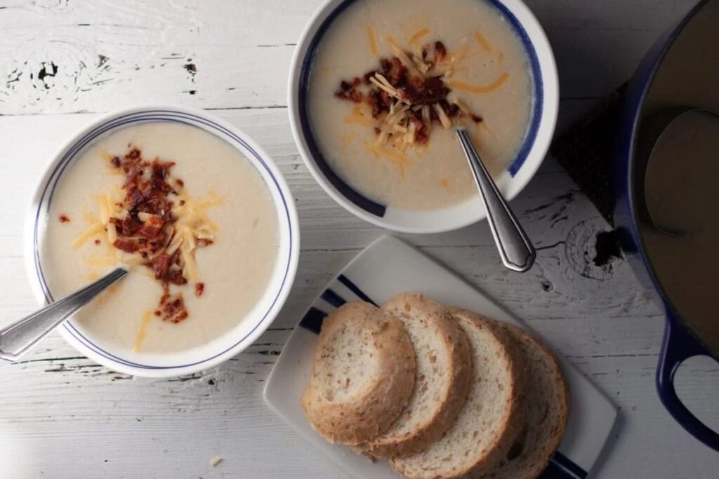 Two bowls of potato soup with bacon and cheese, served with bread.