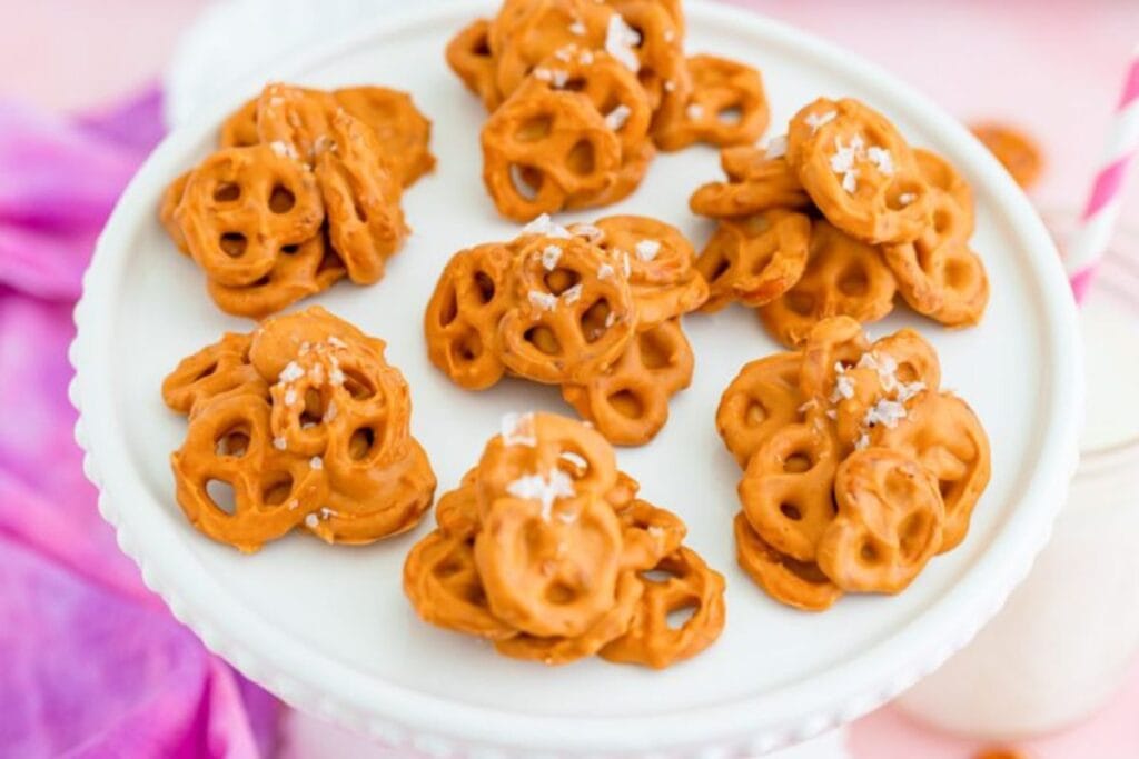 Clusters of peanut butter coated pretzels with sea salt on a white cake stand.