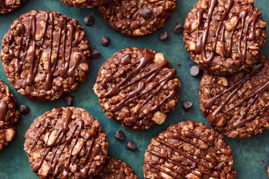 Overhead shot of chocolate oatmeal cookies drizzled with chocolate on a teal background.