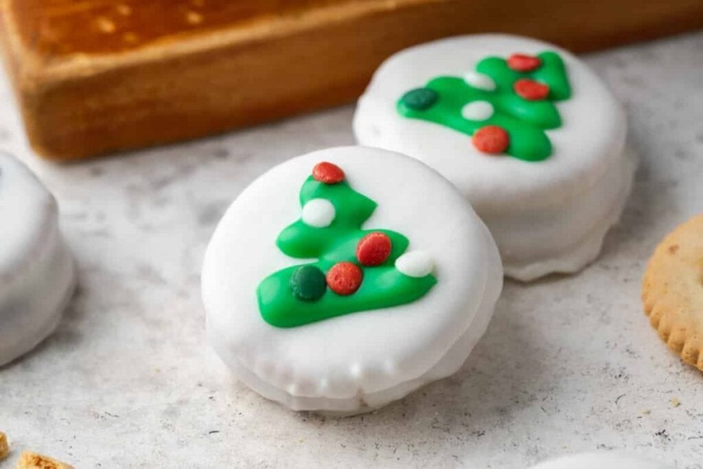 Two white frosted cookies decorated with green Christmas trees and colorful candy dots.