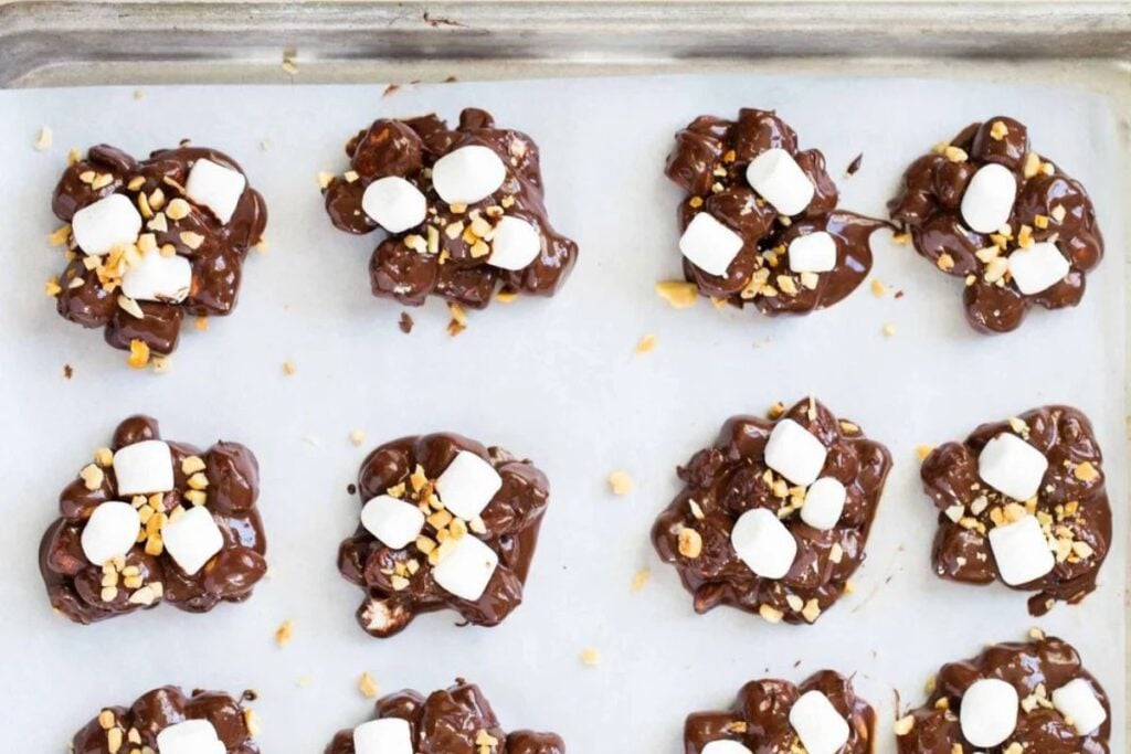 Rocky road candy clusters with chocolate, marshmallows, and nuts on parchment paper.