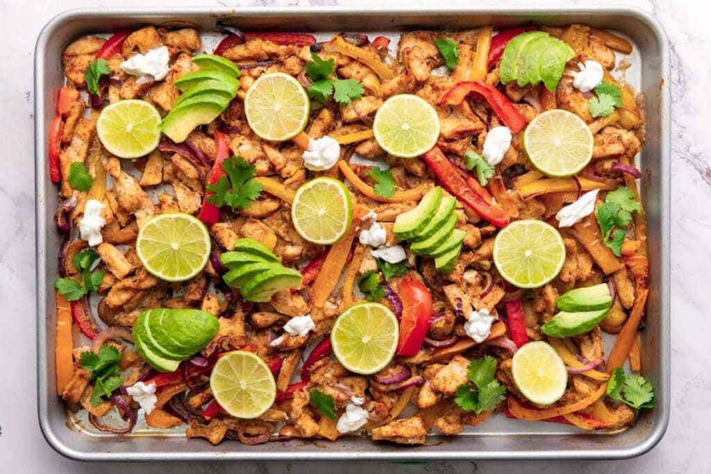 Chicken fajitas on a sheet pan, topped with avocado, lime, and cilantro.