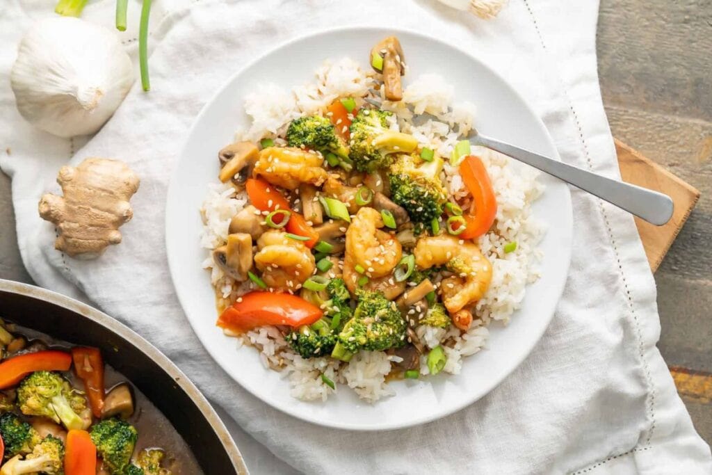 Plate of shrimp stir-fry with rice, broccoli, carrots, and mushrooms.
