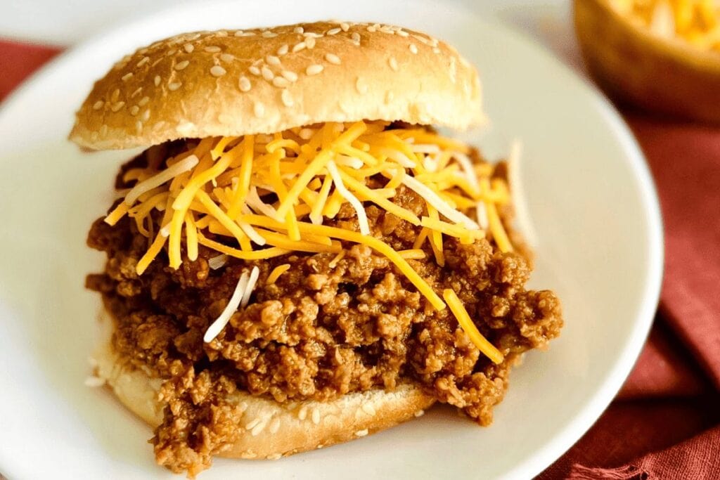 Sloppy Joe sandwich on a sesame seed bun with shredded cheese.