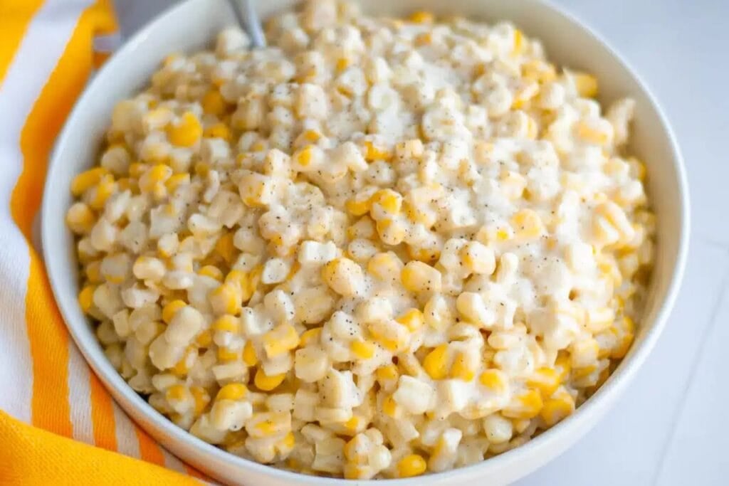 A bowl of creamed corn with a yellow and white striped cloth.