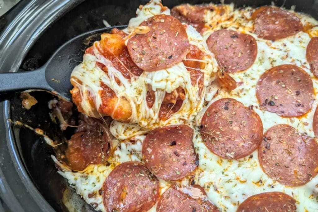 Spoon lifting a cheesy casserole with pepperoni and gnocchi.