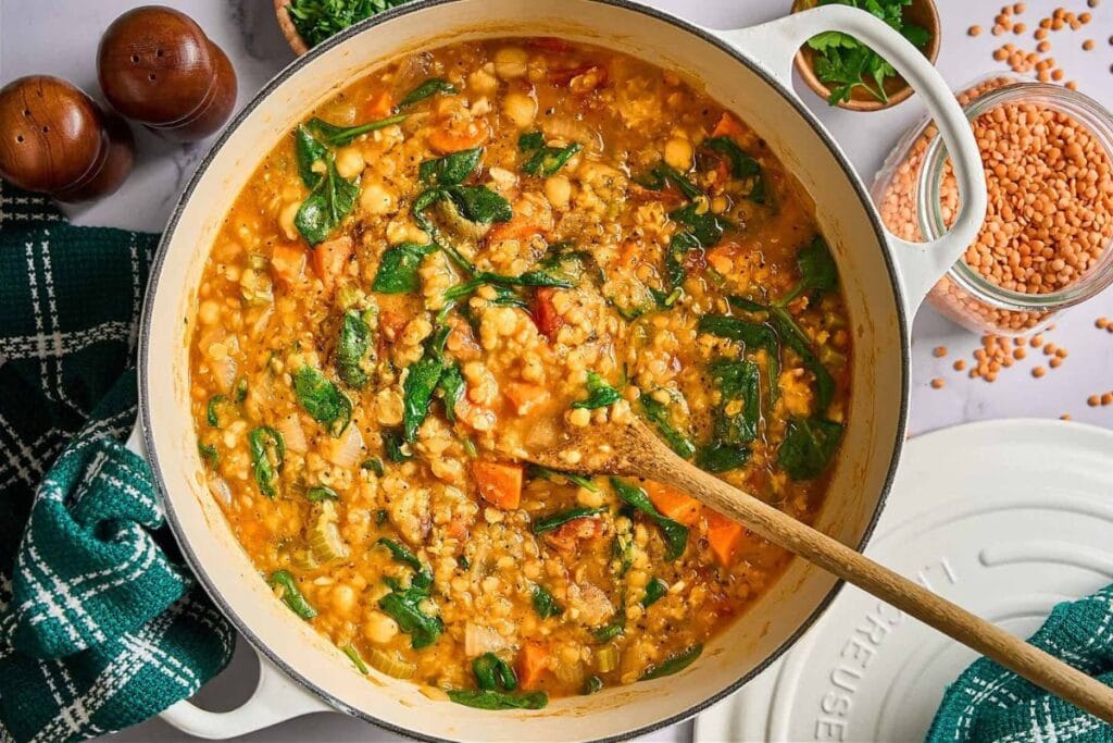 Lentil stew with spinach and chickpeas in a white pot with a wooden spoon.