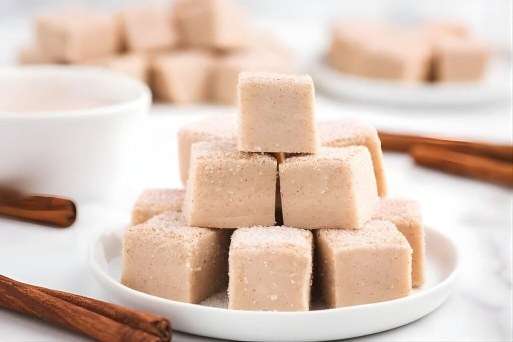 Cinnamon-sugar-coated snickerdoodle fudge squares stacked on a white plate.
