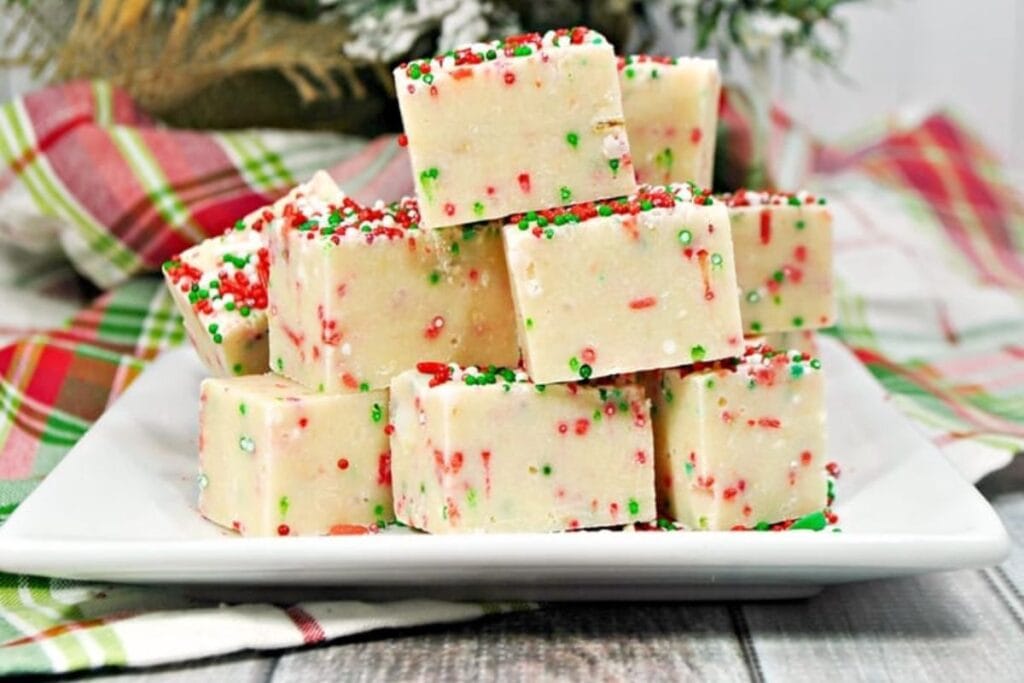 Christmas fudge squares stacked on a white plate with red and green sprinkles.