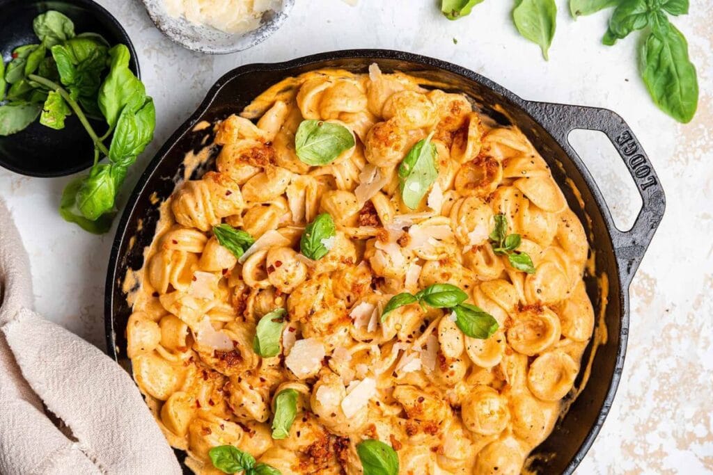 Overhead shot of orecchiette pasta with creamy sauce, basil, and parmesan in skillet.