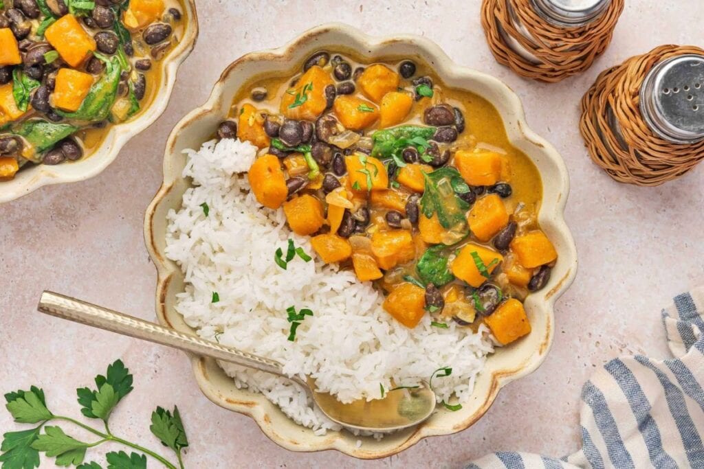 Bowl of rice topped with sweet potato, black beans, and spinach curry.