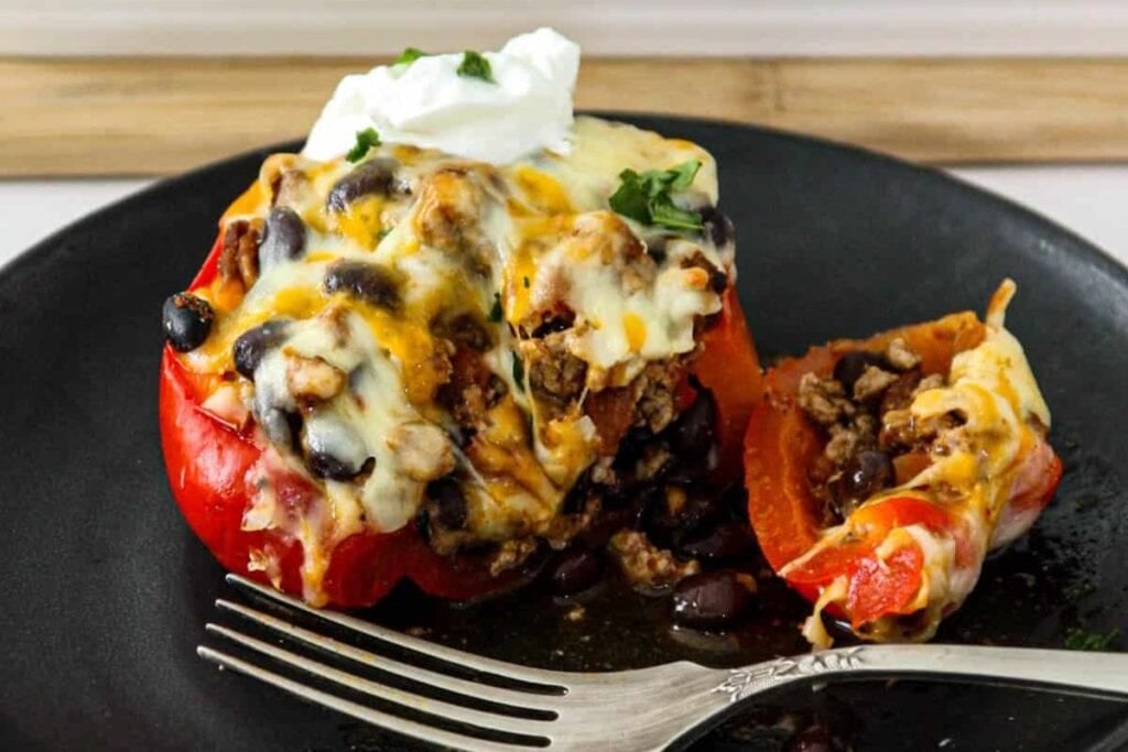 Stuffed bell pepper with taco filling, cheese, and sour cream on a plate.