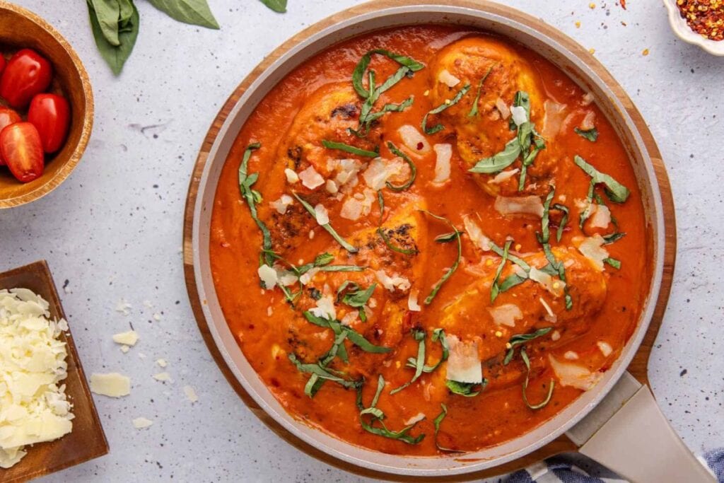 Pan of chicken in tomato sauce with basil and parmesan cheese.