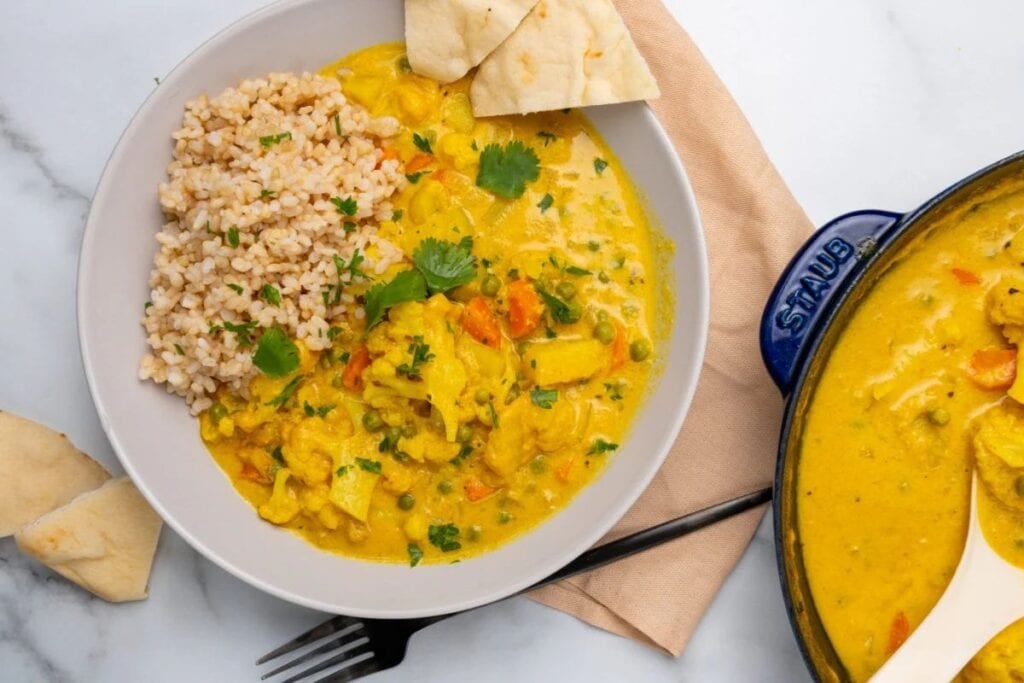 Overhead shot of vegetable korma with rice and naan bread, next to pot.