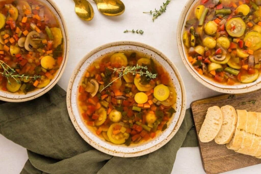 Three bowls of vegetable soup with bread slices.