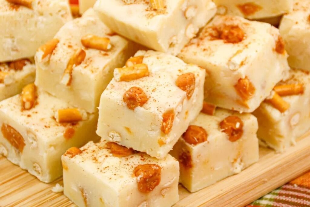 Pile of white fudge squares with caramel pieces on a wood board.