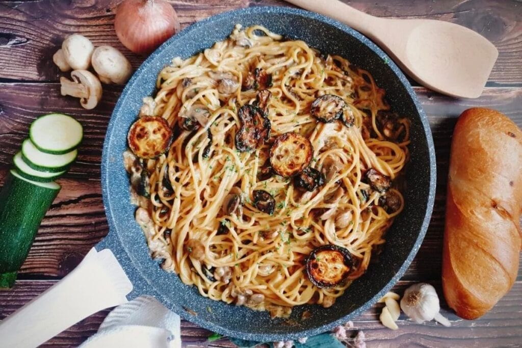 Overhead shot of zucchini mushroom pasta in a pan with bread and ingredients.