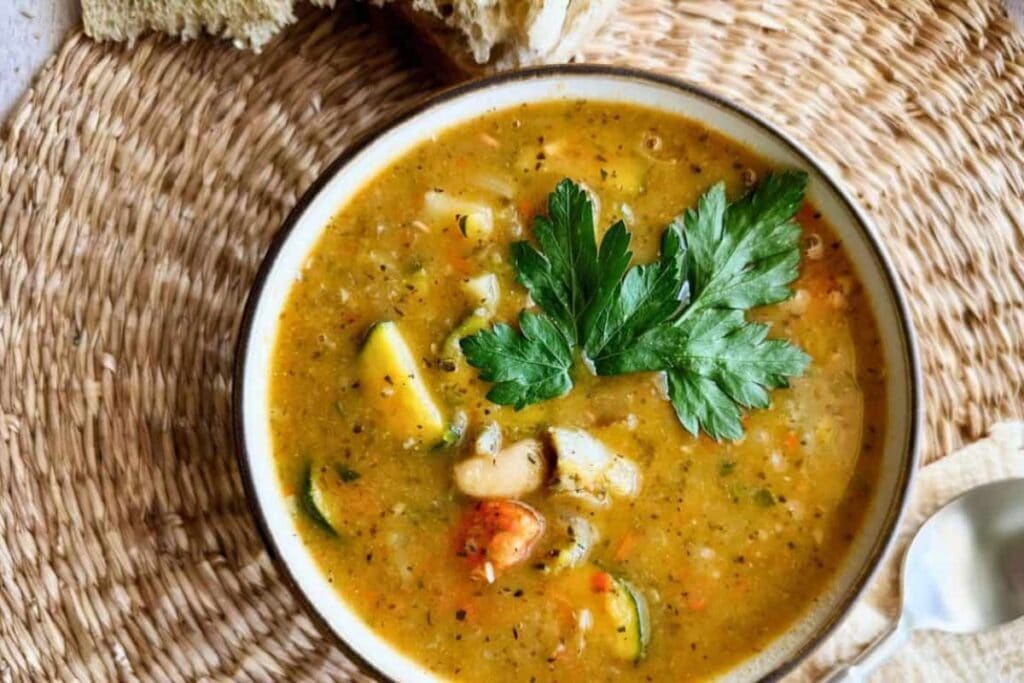 Bowl of vegetable soup with zucchini, potato, beans, and parsley.