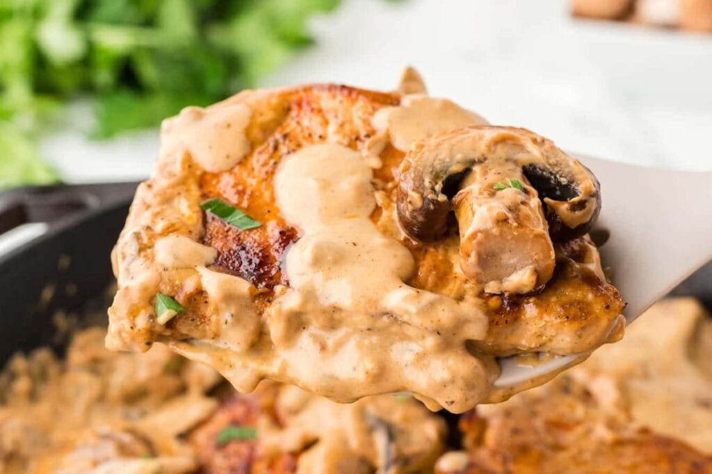 Close-up of pork chops in creamy mushroom sauce on a spoon.
