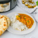 Butter chicken served over rice next to warm naan and a slow cooker.