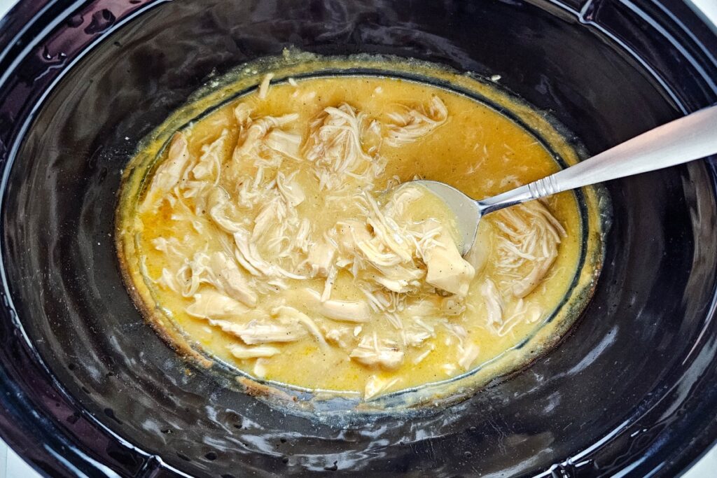 Shredded chicken and gravy in a slow cooker with a spoon.