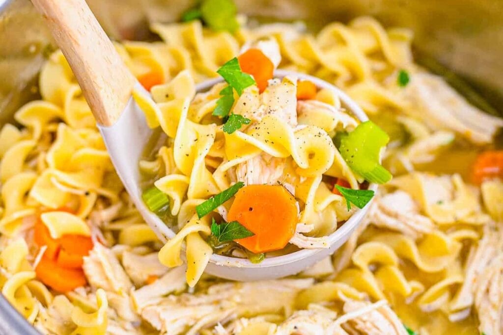 Chicken noodle soup being scooped with a ladle.