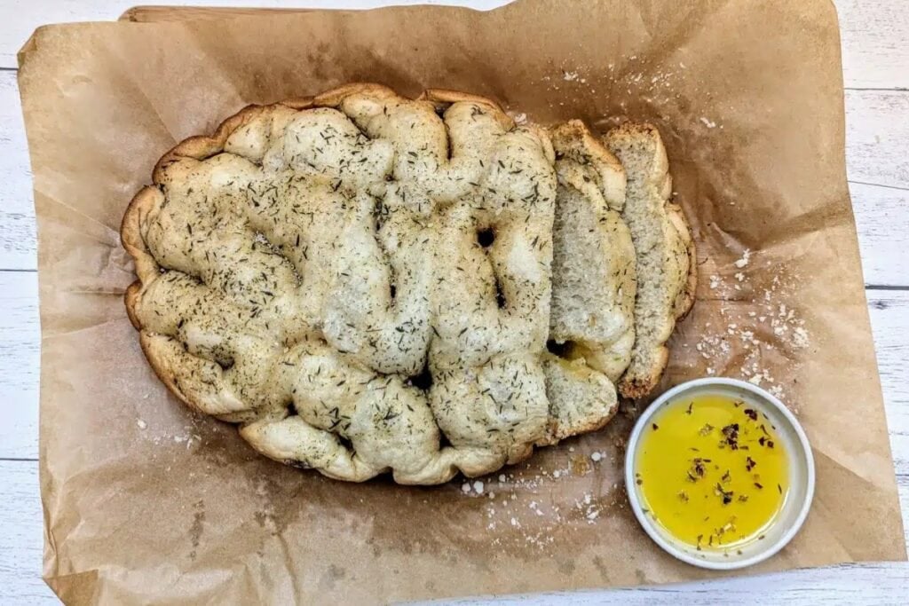 Slow cooker herbed focaccia bread on parchment paper with olive oil for dipping.
