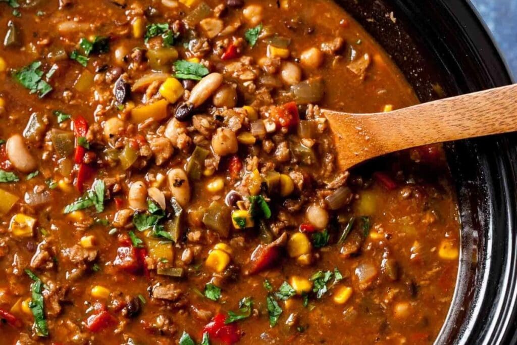 Vegetable and bean chili in a pot with a wooden spoon.