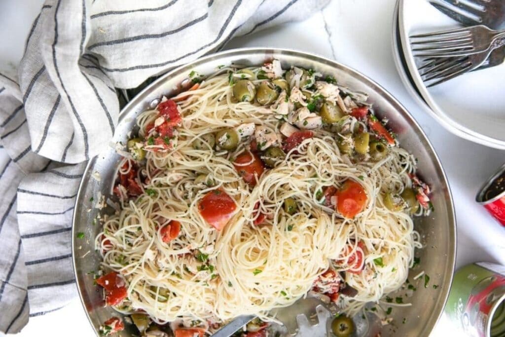 Overhead view of angel hair pasta salad with chicken, tomatoes, and olives in a metal bowl.