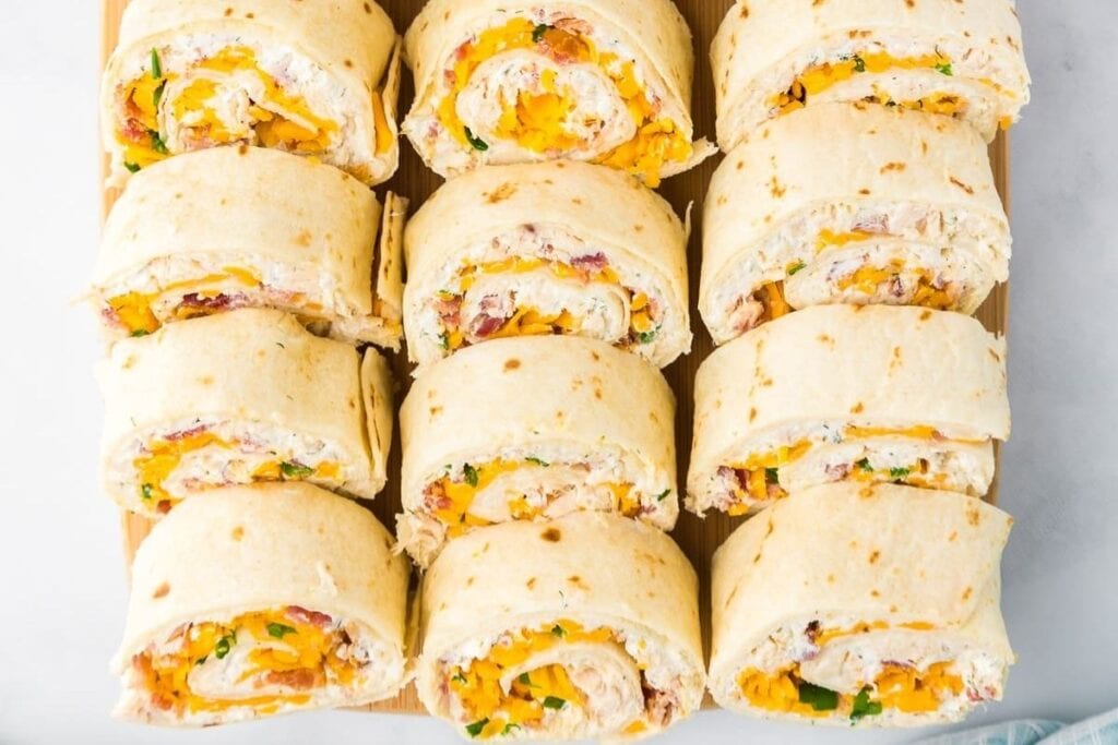 Overhead view of sliced chicken bacon ranch pinwheels on a wooden cutting board.