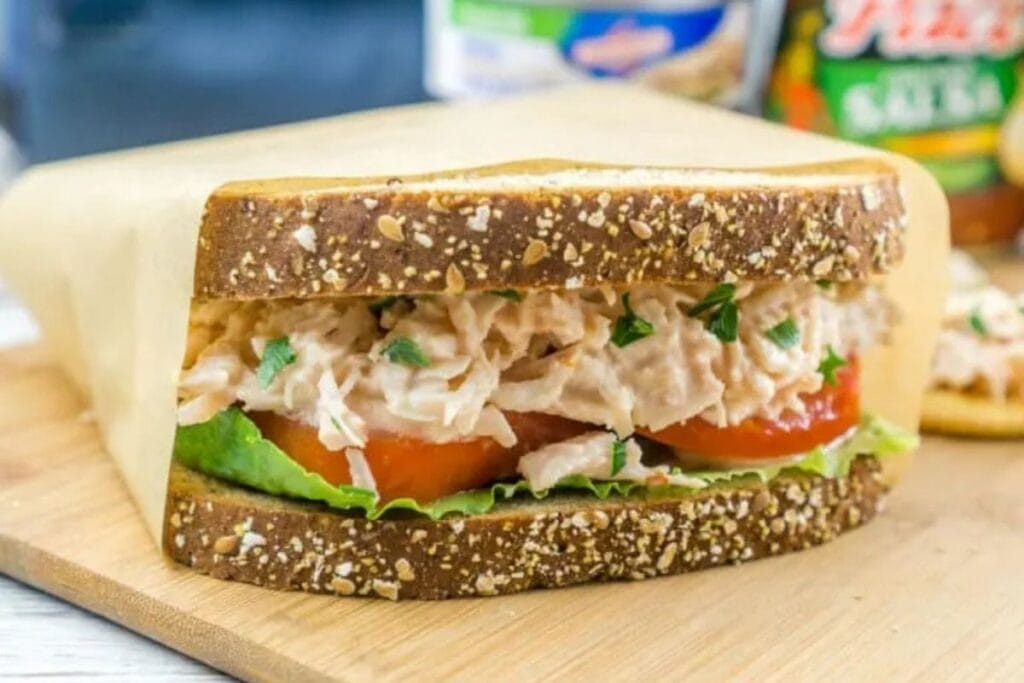 Chicken salad sandwich with tomato and lettuce on whole wheat bread, wrapped in paper.