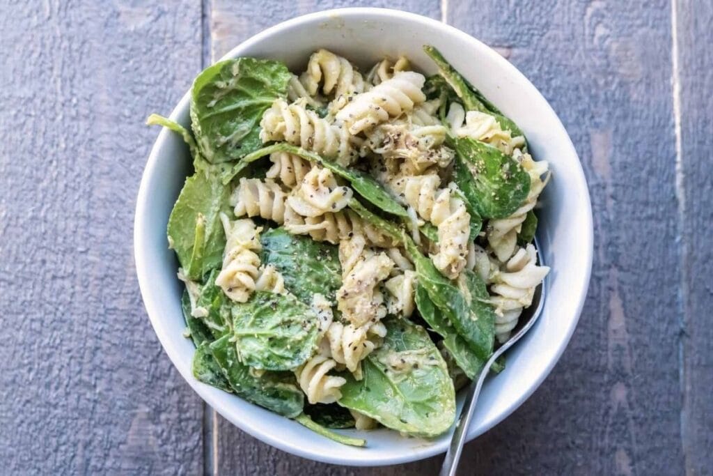 Overhead shot of pasta salad with spinach and a creamy sauce in white bowl.