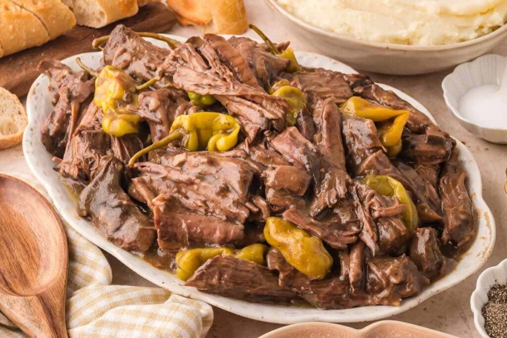 Shredded pot roast topped with whole pepperoncini peppers on an oval serving platter.