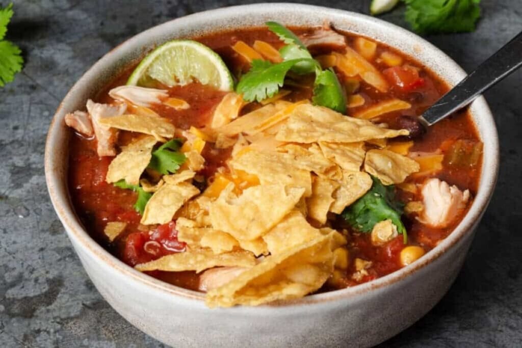 Bowl of taco soup with tortilla chips, cilantro, lime, and a spoon.