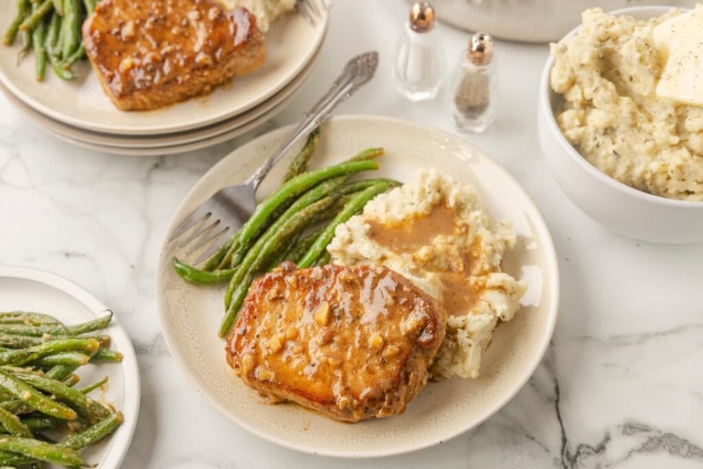 Apple cider glazed pork chop with green beans on a plate.