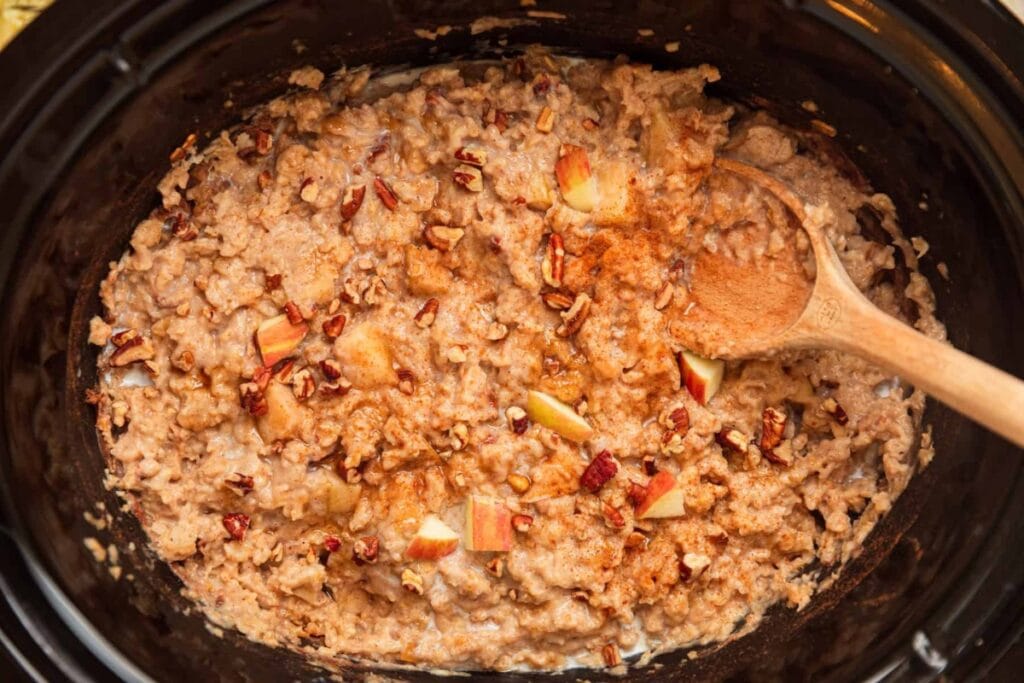 Apple pie oatmeal in a slow cooker with chopped apples, pecans, and cinnamon.