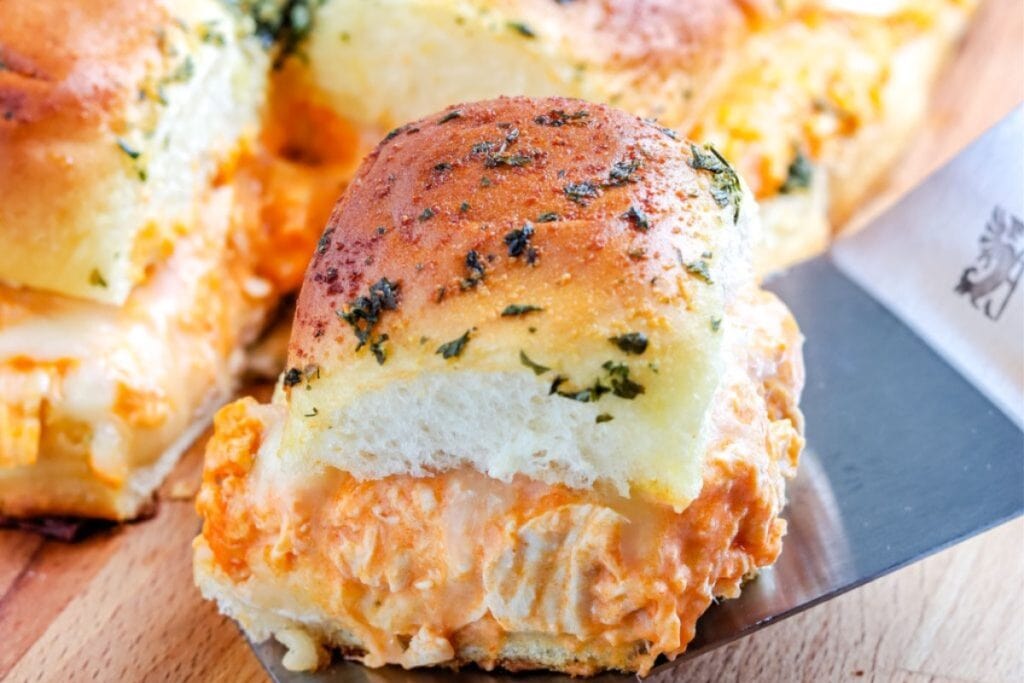Buffalo chicken sliders with creamy filling on a spatula.